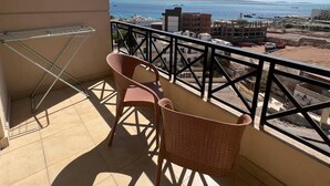 A balcony with two wicker chairs and a metal drying rack. The balcony overlooks a coastal area with buildings and boats.