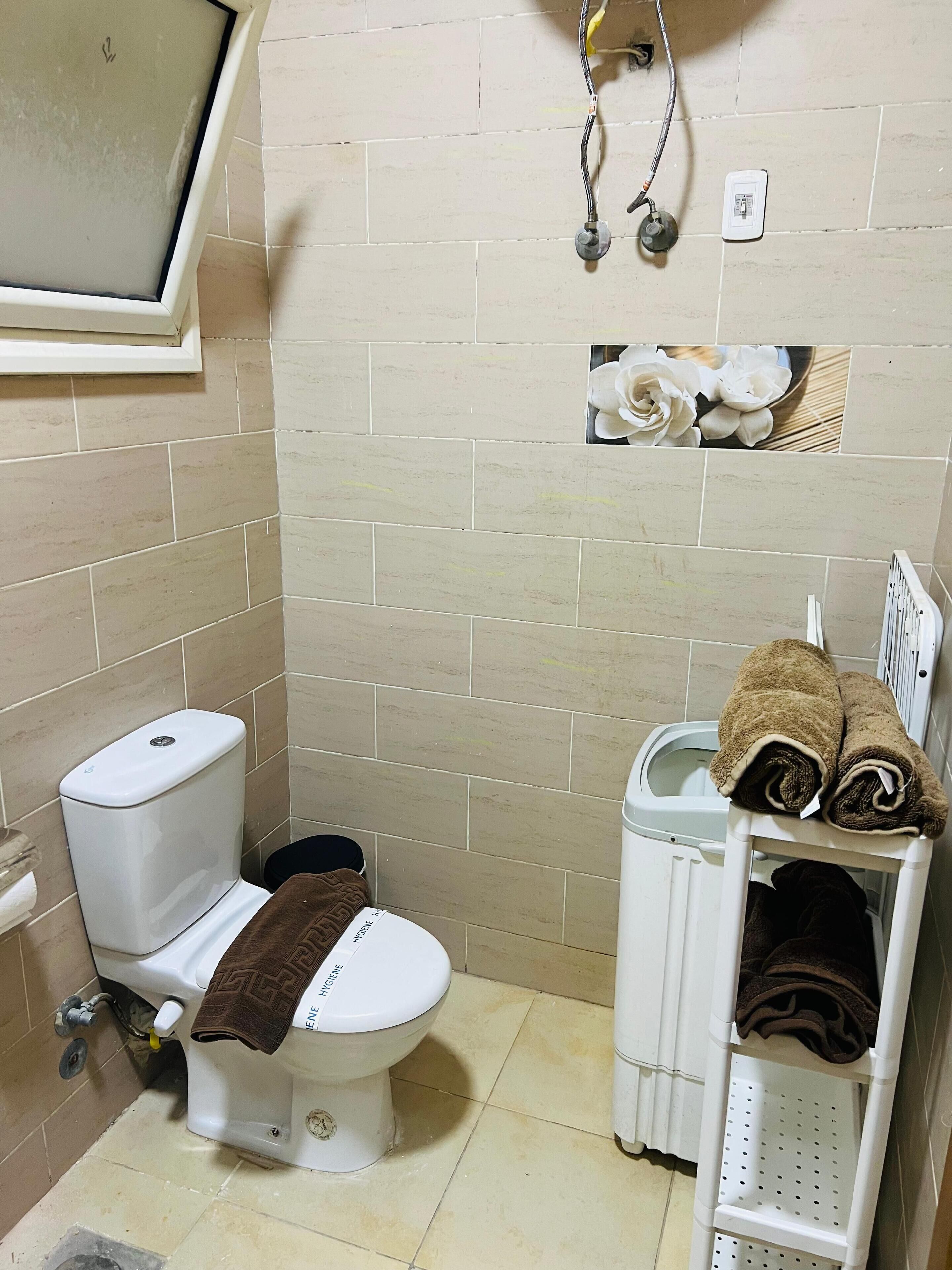 Une petite salle de bain avec des toilettes, une poubelle et une étagère avec des serviettes.
