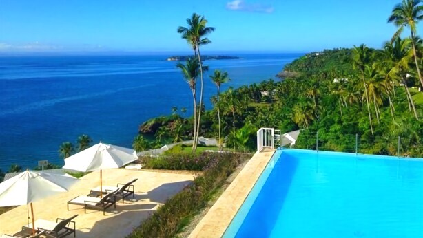 A poolside area with lounge chairs and umbrellas, overlooking a beach and ocean. - Vista Mare Samana Ocean View Top Floor 1 Bed (Samaná)