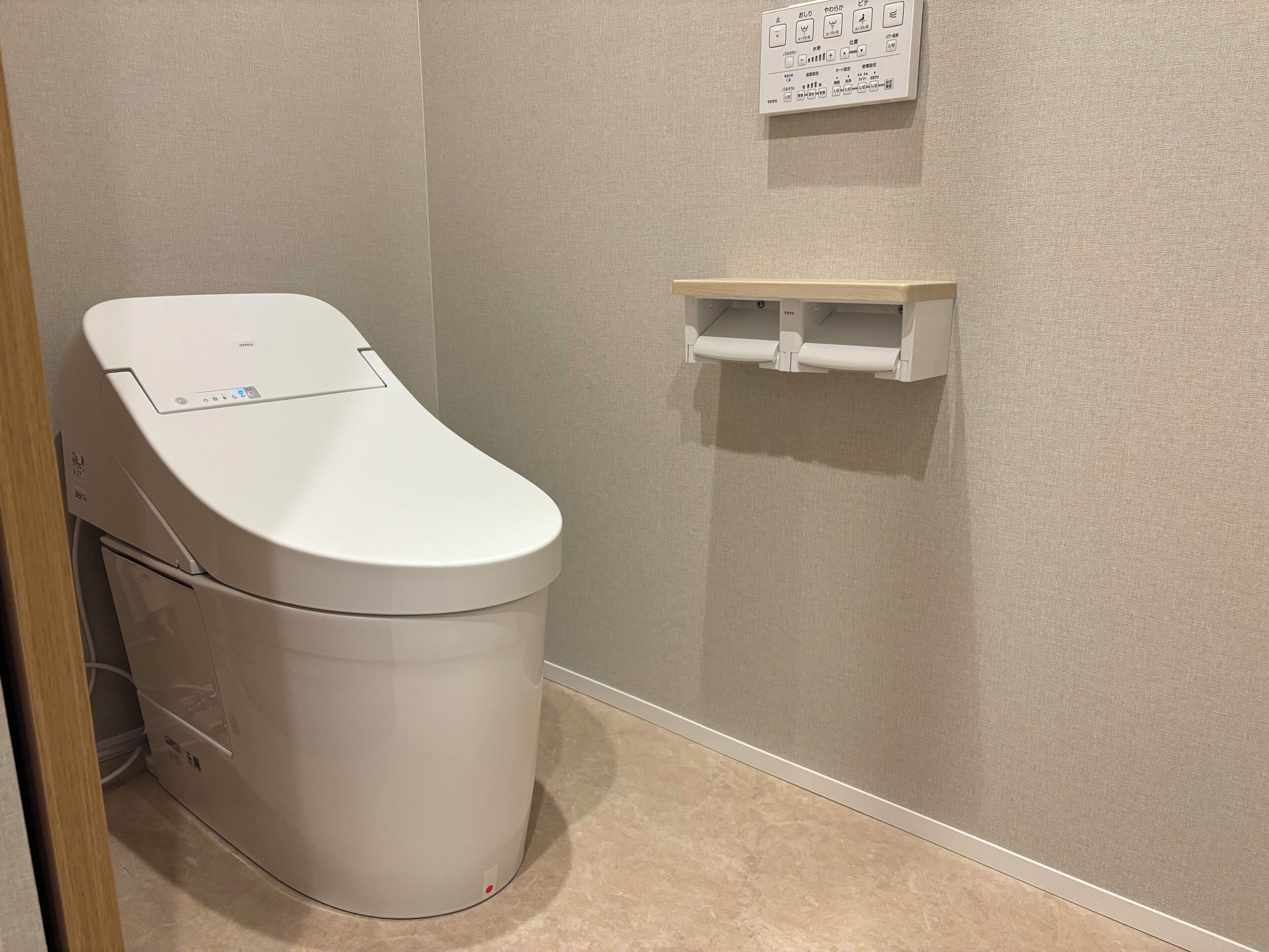 WC, jossa on ohjauspaneeli, seinälle kiinnitetty hylly ja ovenkarmi.
