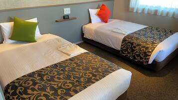 Two single beds with patterned bedspreads, a control panel on the wall, and a window with curtains.