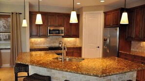 A kitchen with granite countertops, a built-in island with bar stools, wooden cabinets, and pendant lighting. - 3/2.5 home, custom designed with vacation in mind. (Marco Island)