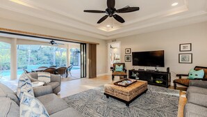 A spacious living room with a large TV, comfortable seating, and a view of a swimming pool. - 3/2.5 home, custom designed with vacation in mind. (Marco Island)