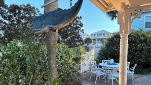 Un espace patio avec une table et des chaises blanches, entouré de verdure et agrémenté d’une sculpture décorative représentant un requin.