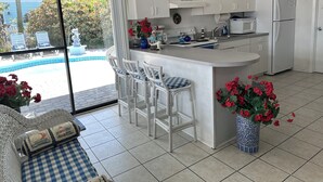 Une cuisine dotée d’un îlot central, de meubles blancs, d’un réfrigérateur et donnant sur une piscine.