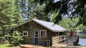 Eine kleine Holzhütte mit einer blauen Tür, einer Veranda und einem Steg, der in einen See führt.