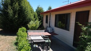 Eine Terrasse mit Tisch und Stühlen, einer kleinen Klimaanlage und einem Fenster mit Moskitonetz.