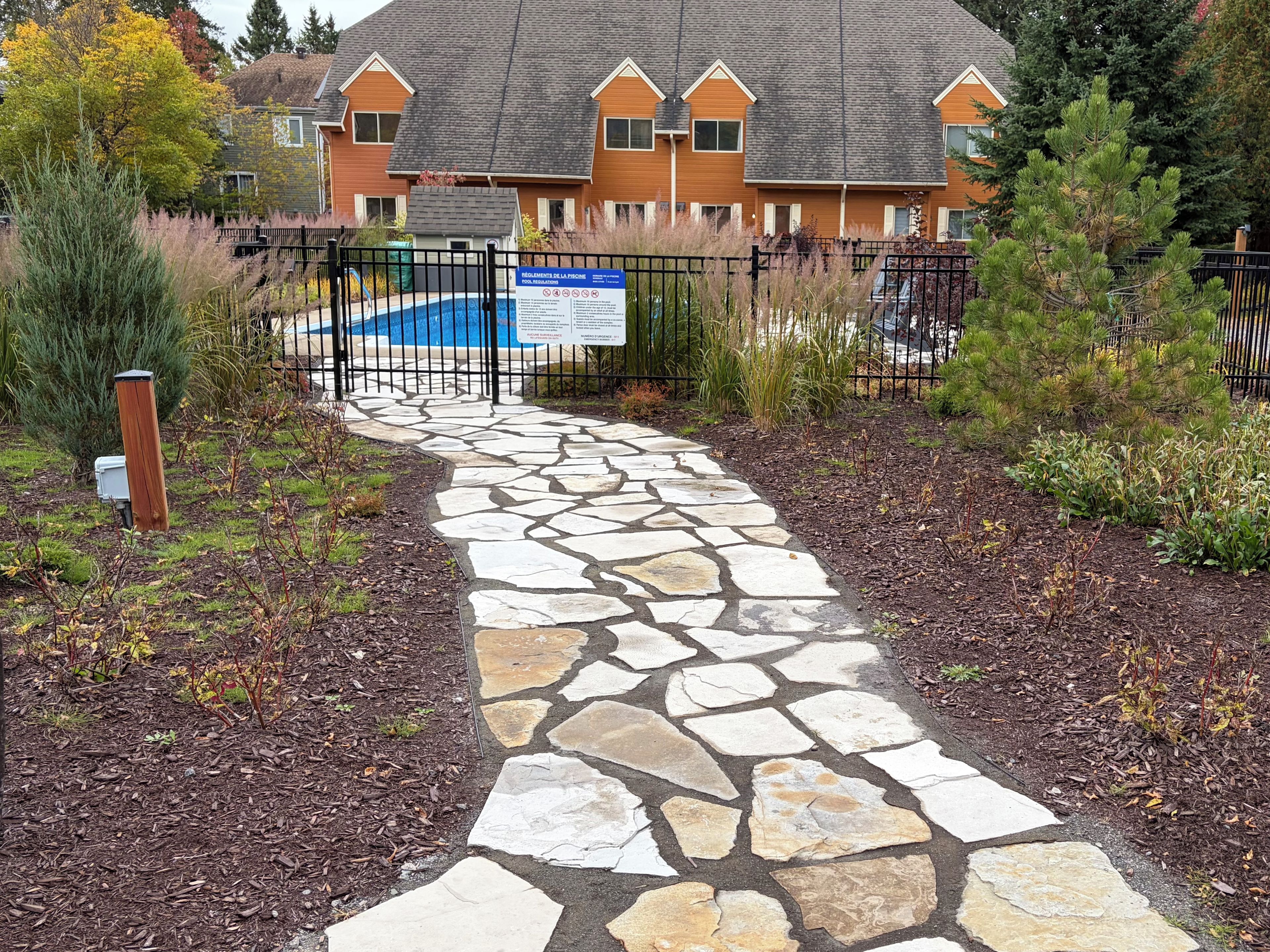 A stone pathway leading to a pool area, surrounded by a fence and a sign with regulations.