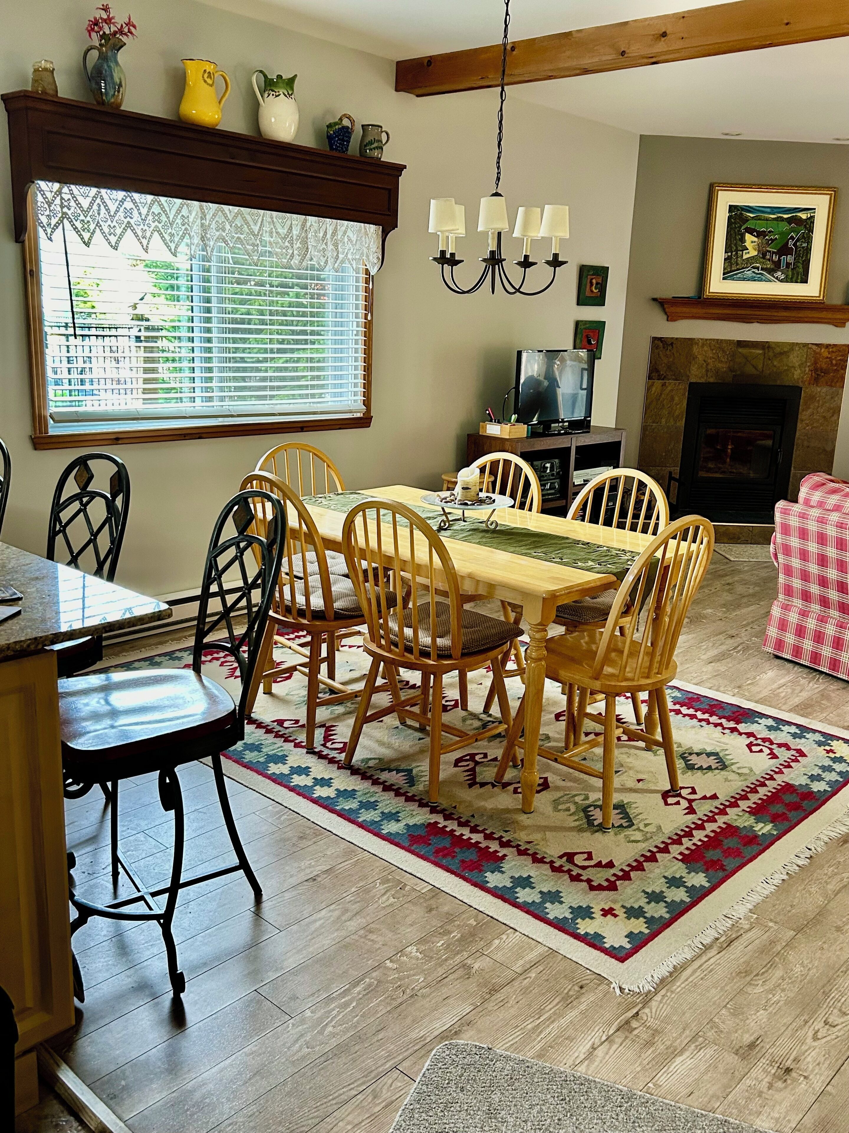 A dining area with a wooden table and chairs, a patterned rug, and a fireplace.
