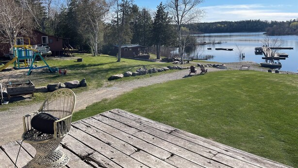 A lakeside property with a wooden deck, a children's play area, and a dock with boats.