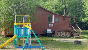 A wooden cabin with a slide, a small deck, and a grill area.