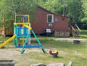 A wooden cabin with a slide, a small deck, and a grill area.