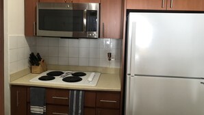 Una cocina con gabinetes de madera, un microondas de acero inoxidable, un refrigerador blanco, una estufa y un salpicadero de azulejos.