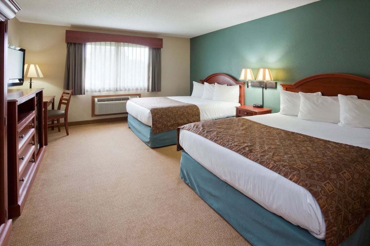 A hotel room with two beds, a desk, a chair, a TV, and a window with curtains.