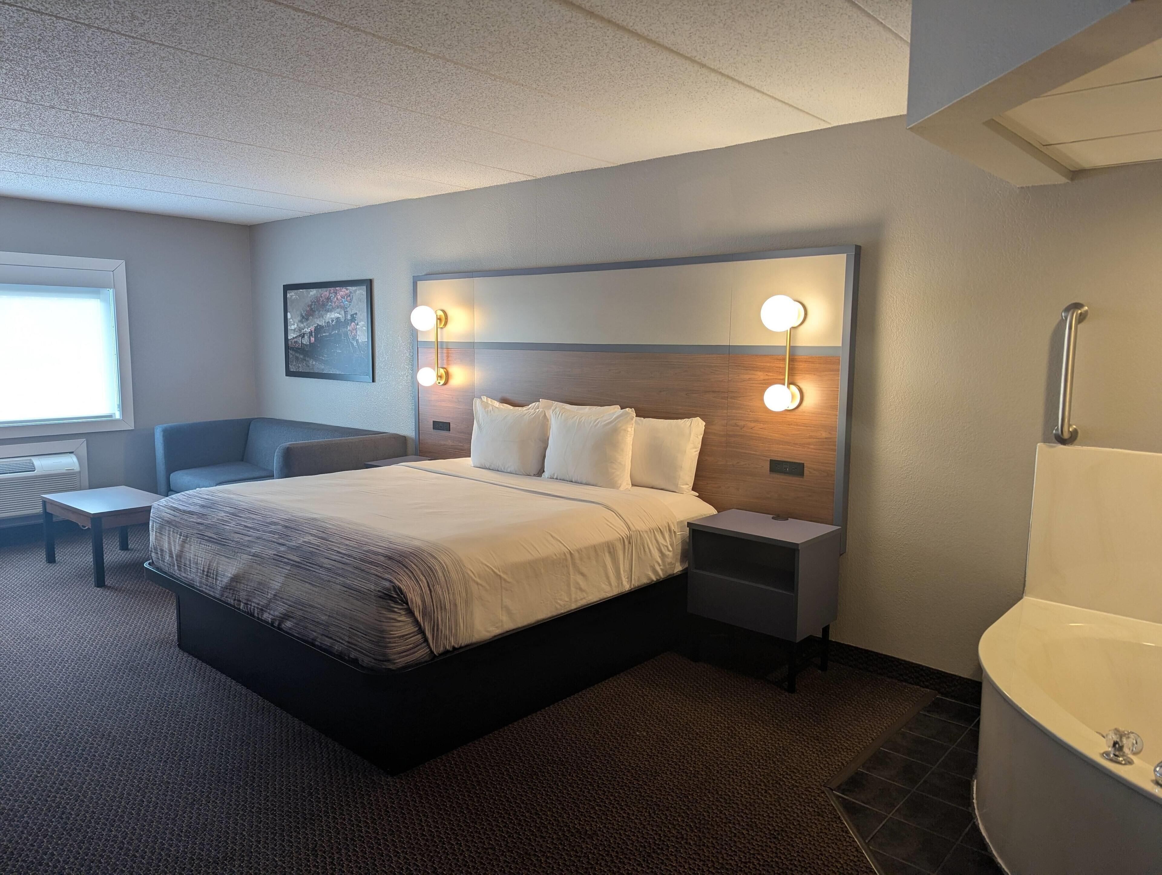 A modern hotel room with a large bed, bedside tables, a desk, and a bathroom with a bathtub.