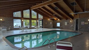 Una piscina interior con vistas despejadas al exterior a través de amplias ventanas, rodeada de asientos y un techo de madera.
