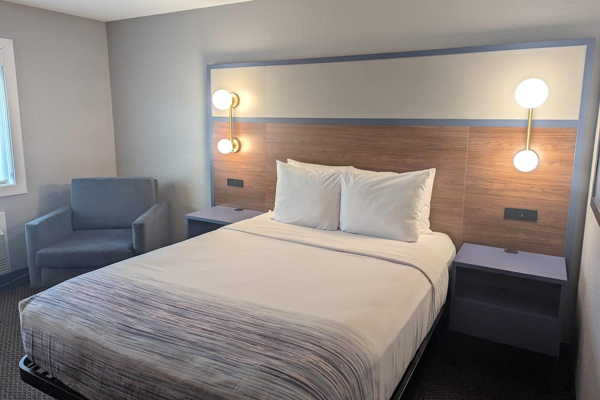 A hotel room with a large bed, two bedside tables, a chair, and wall-mounted lighting.