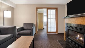 Habitación de hotel con chimenea, televisor, sofá y puerta que da a otra habitación.