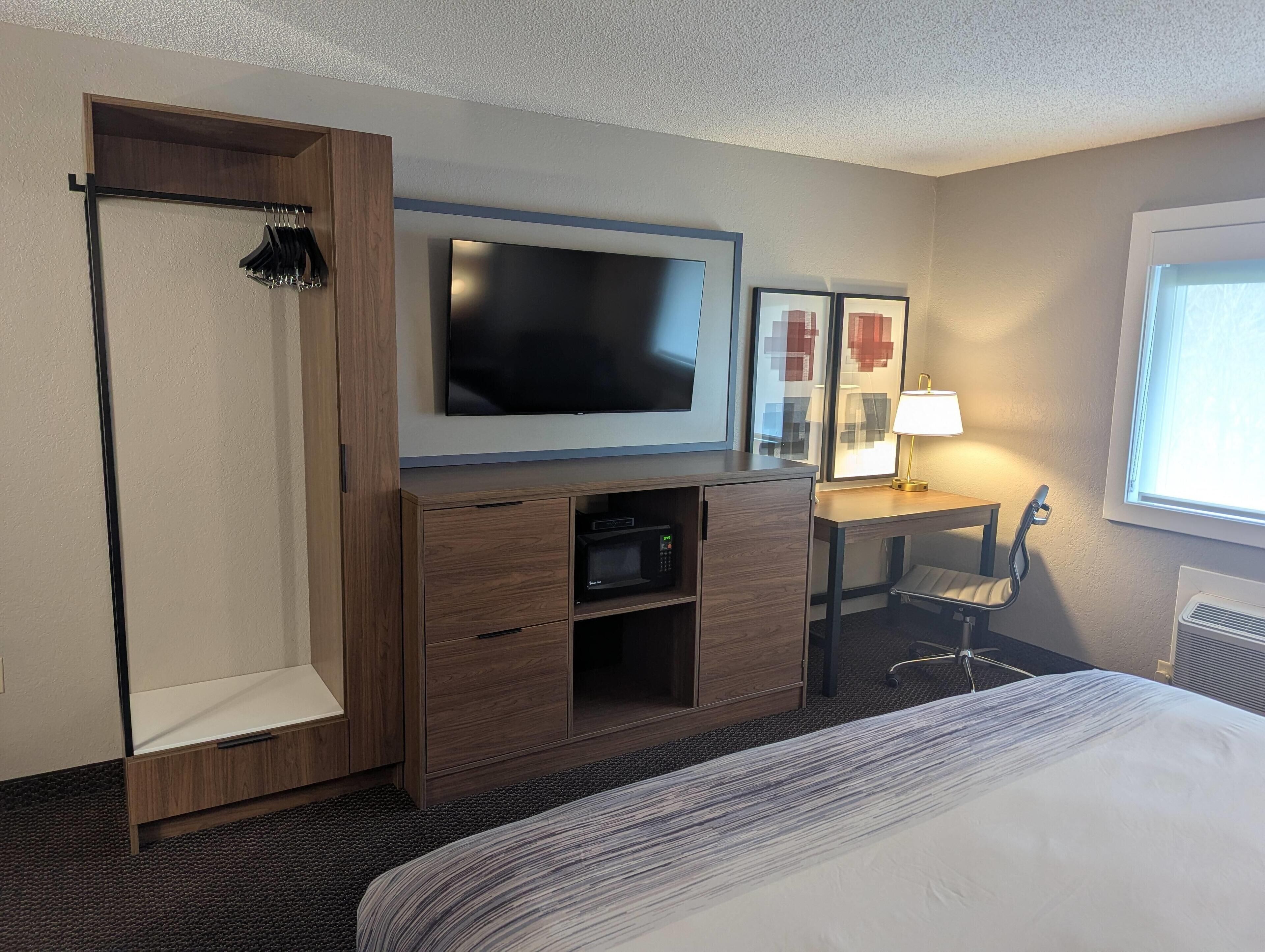 Habitación de hotel con cama, televisión montada en un mueble de madera, escritorio con una silla y una ventana.
