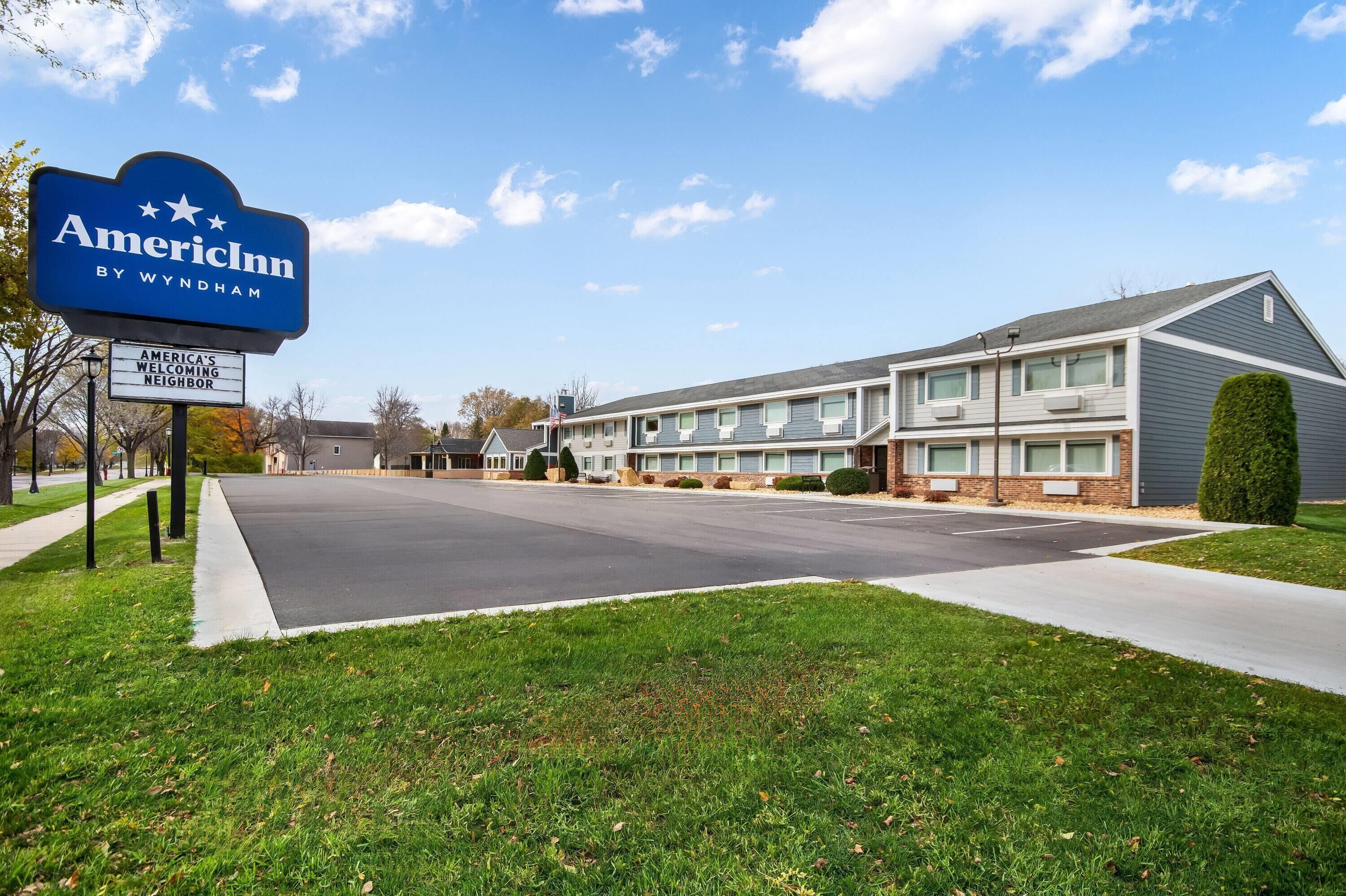 A two-story motel with a sign reading "AmericInn by Wyndham" and a welcoming neighbor sign.