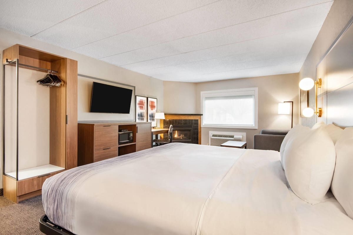 A hotel room with a large bed, a flat-screen TV, a fireplace, a desk, and a wardrobe.