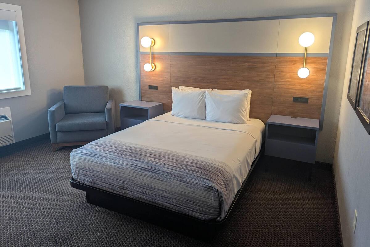 A hotel room with a large bed, two bedside tables, a chair, and wall-mounted lights.