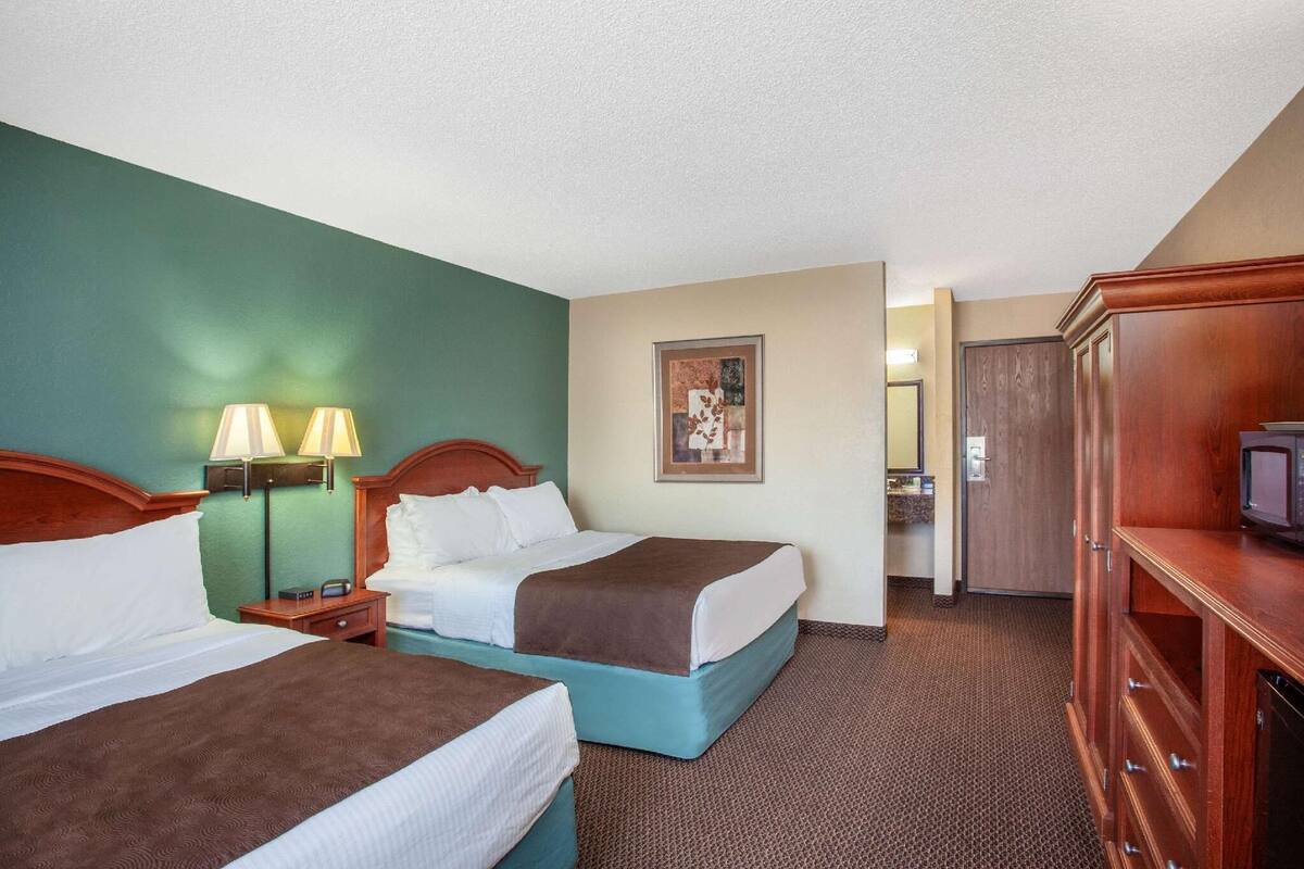 A hotel room with two beds, a TV, a desk, and a bathroom.