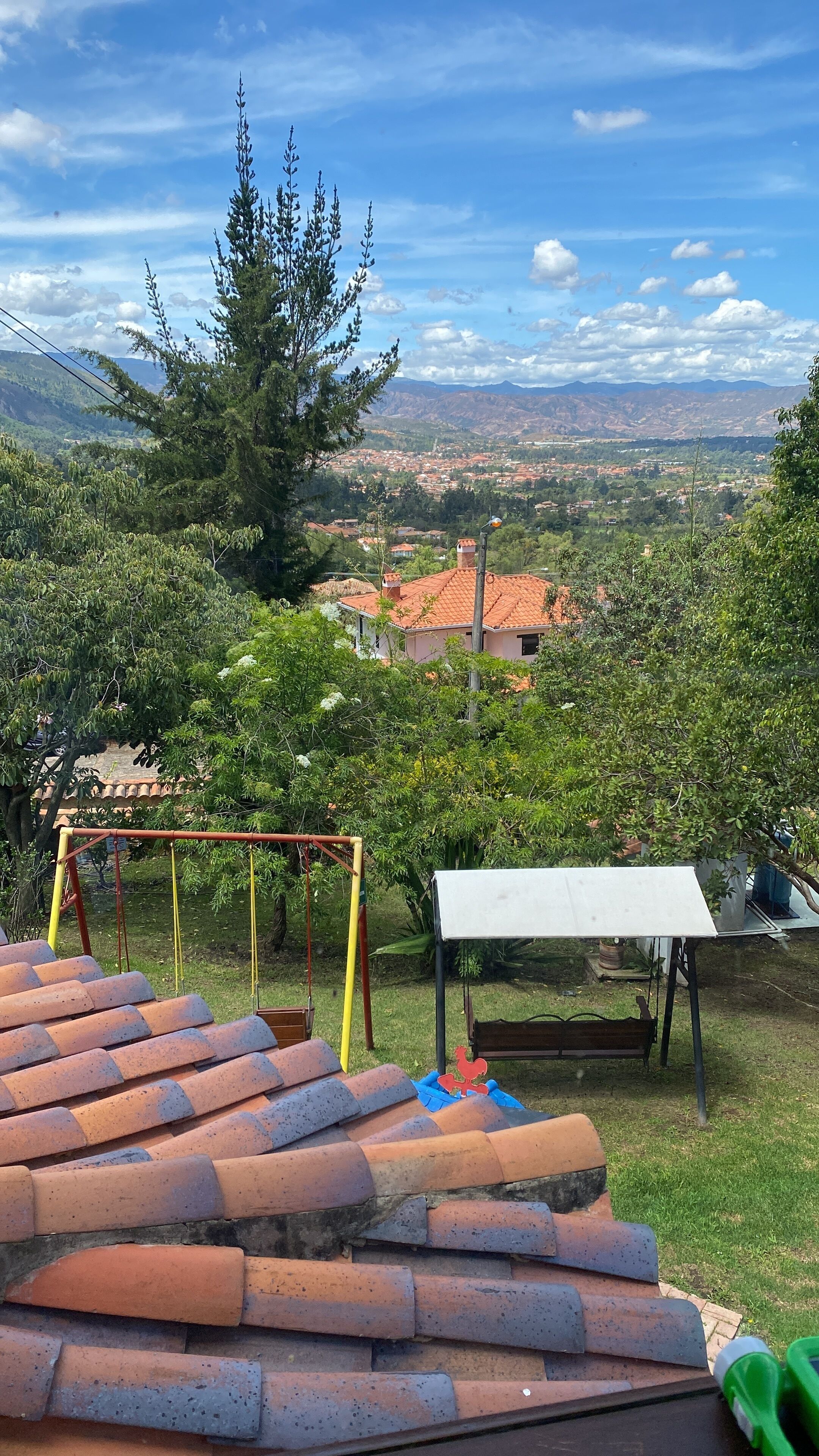 Un patio con una mesa y un columpio, con vista a una zona residencial con casas y montañas al fondo.