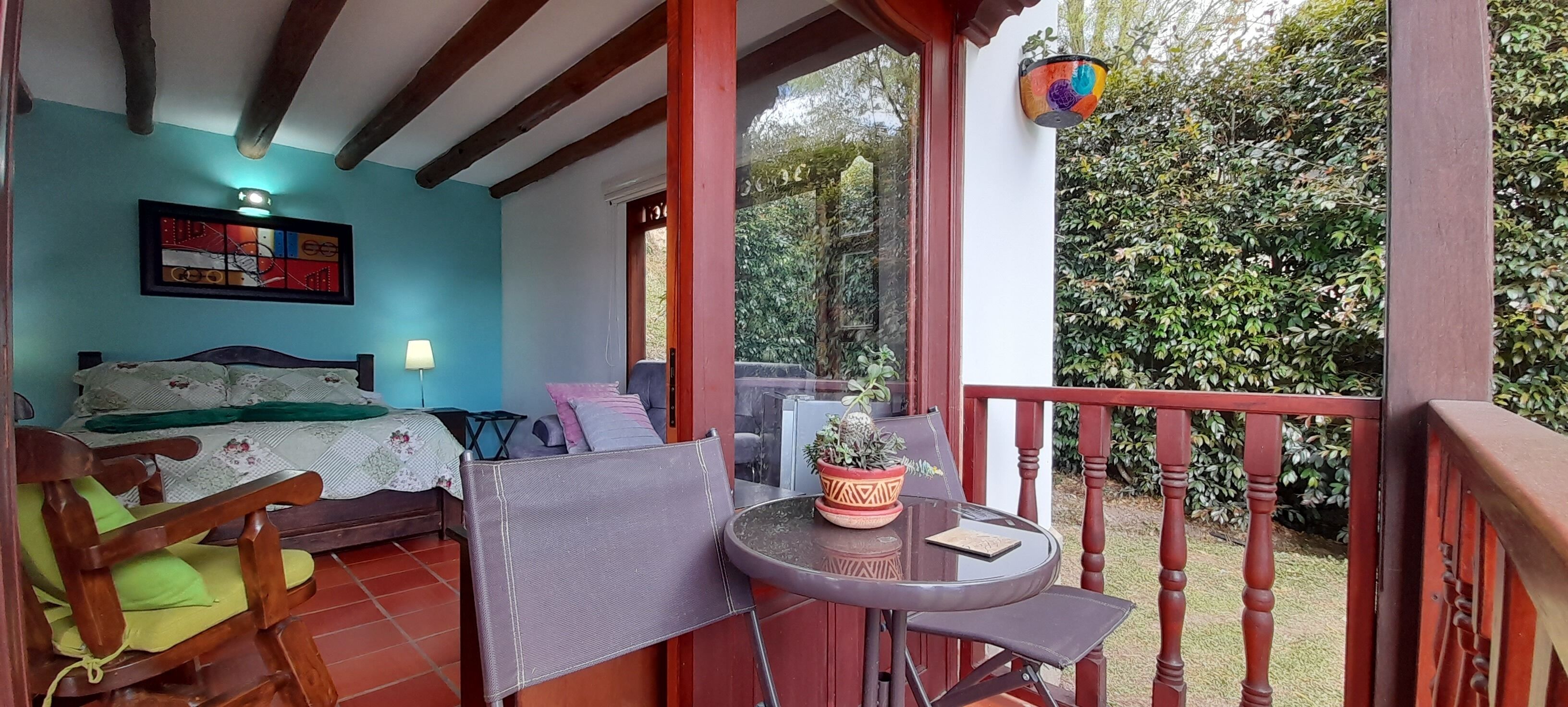Un dormitorio acogedor con cama, una silla, una mesita y un balcón con vistas a zonas verdes.
