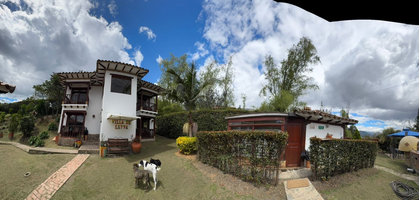 A villa with a white exterior, a balcony, and a small garden area with a pathway leading to the entrance.