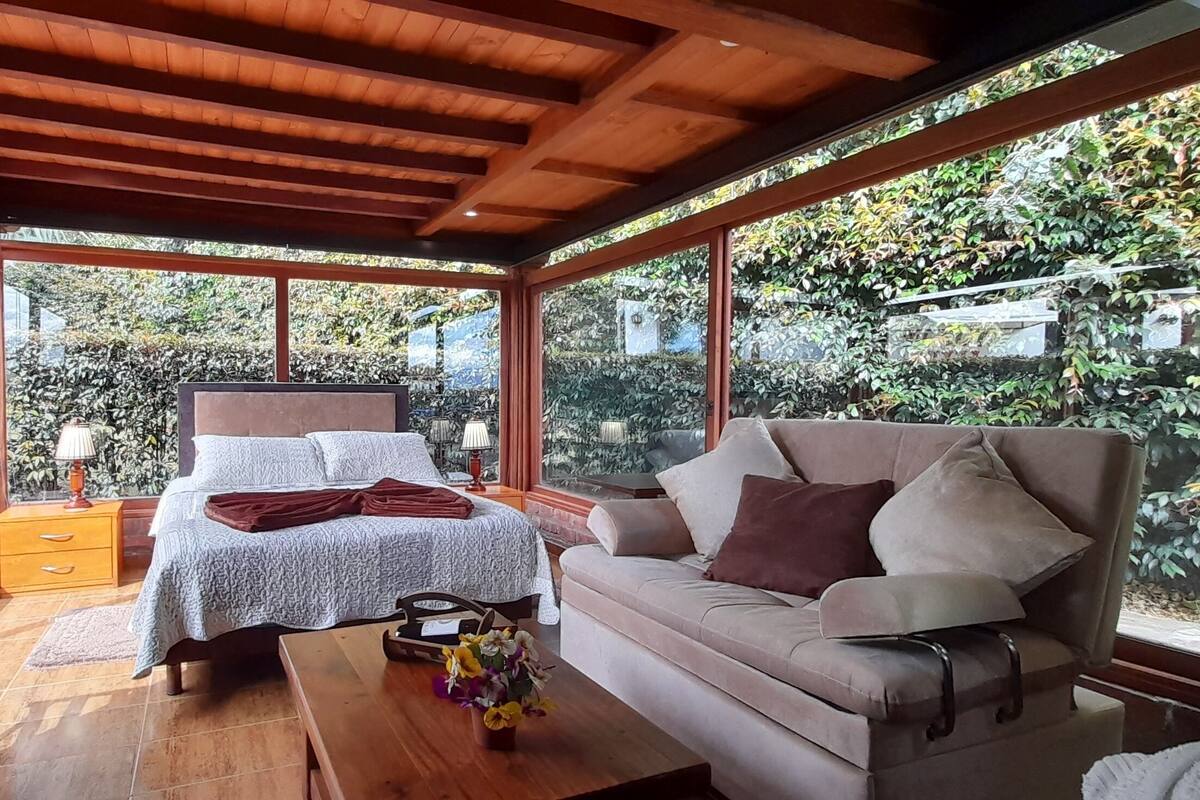 Un dormitorio con cama, sofá, techo de madera y ventanas amplias.