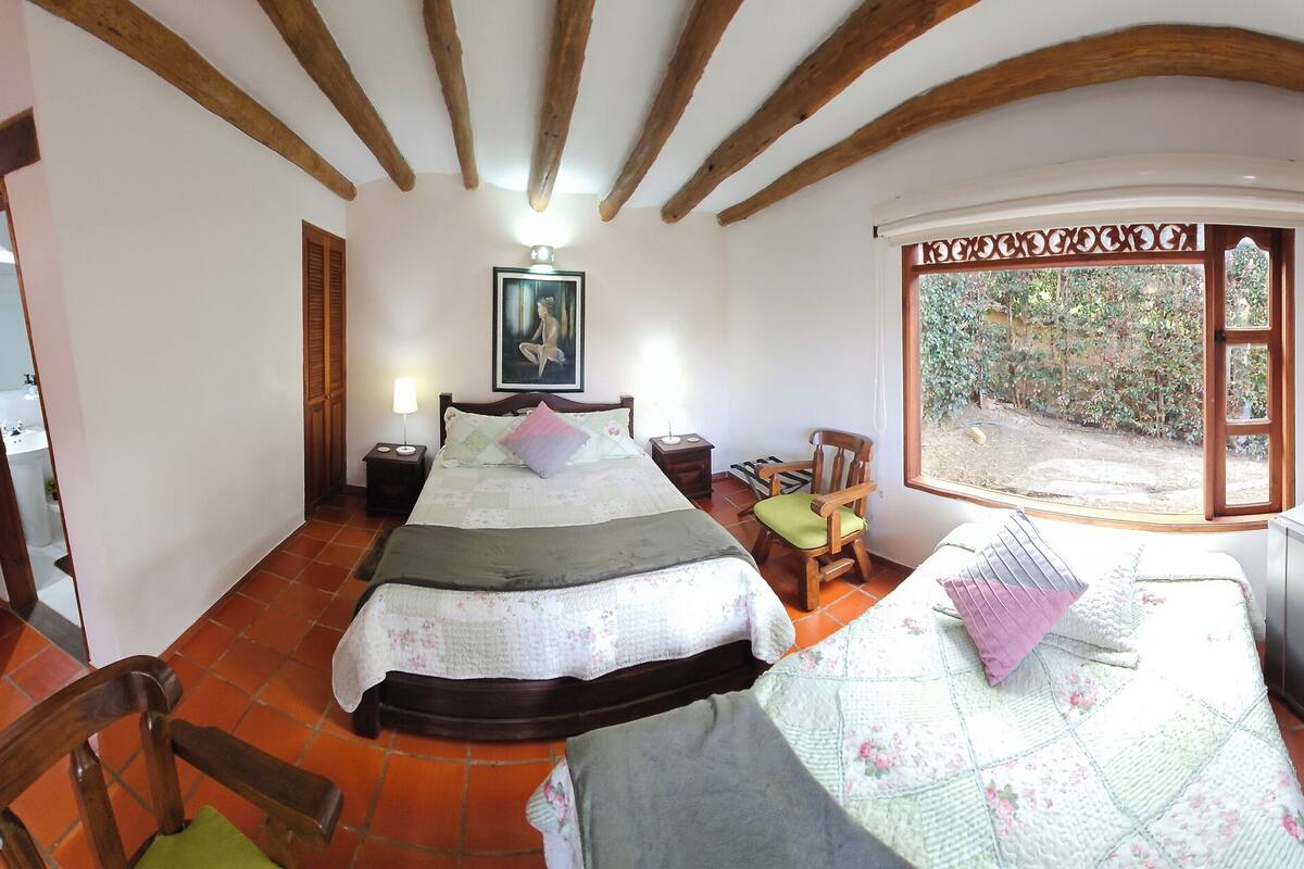 Un dormitorio con cama, televisión, una mesita y un balcón con vistas al jardín.