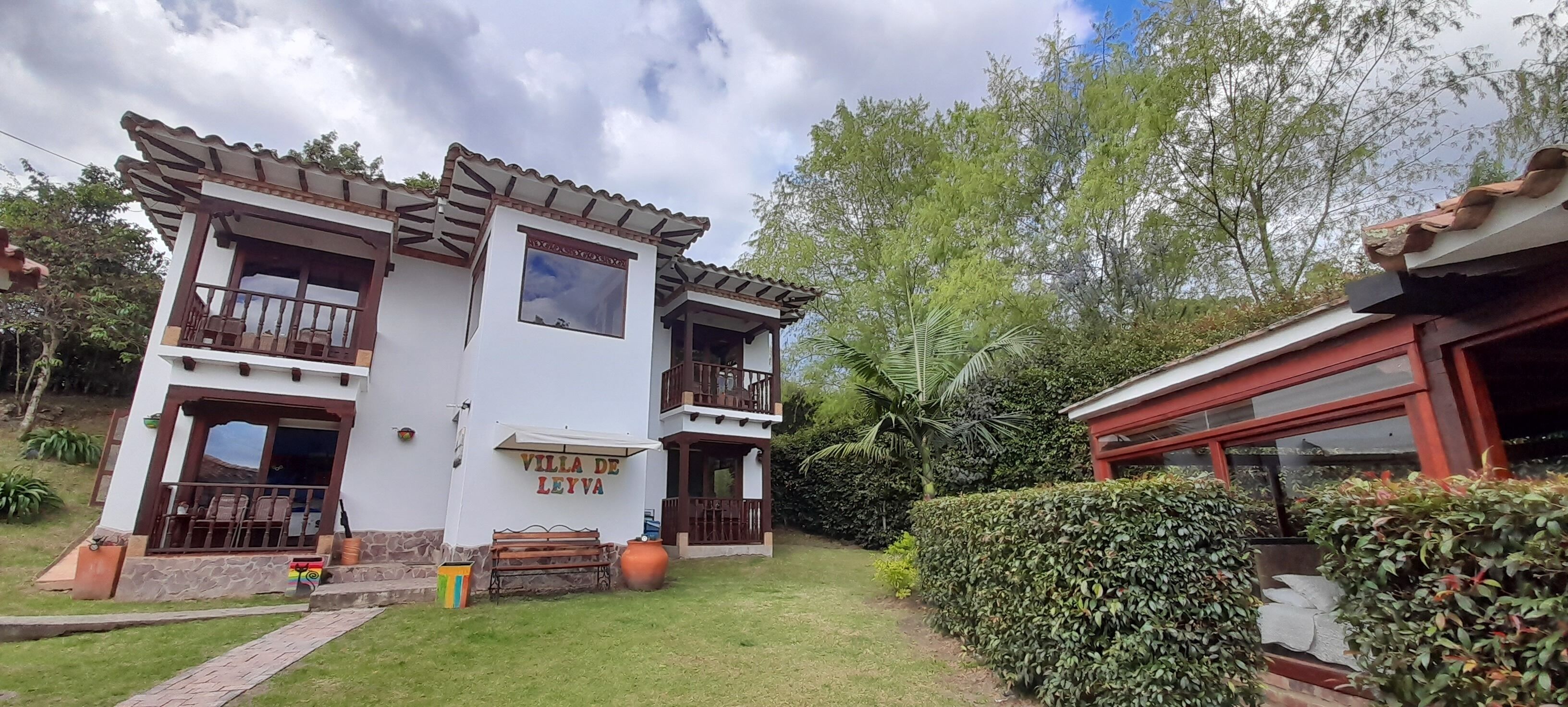 Una villa de dos pisos con balcón, patio y un jardín cuidado.