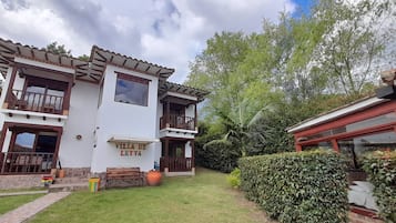 Una villa de dos pisos con balcón, patio y un jardín cuidado.