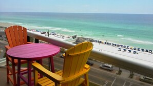 A balcony with a table and chairs overlooking a beach with umbrellas and people. -  So Cozy & Serene Perfect Getaway Gulf Front Studio  
Private  Balcony Bch Srv  (Miramar Beach)