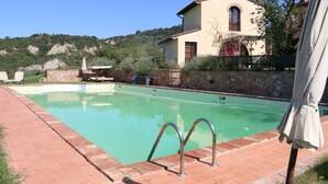 Une piscine avec des garde-corps en métal, un mur en pierre et une maison en arrière-plan.