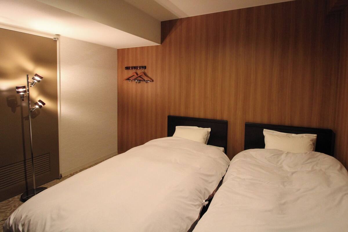 A hotel room with two beds, a wooden wall, a coat rack, and a floor lamp.