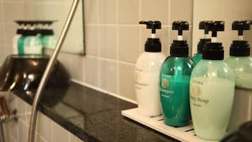 Une salle de bain équipée d’une douche, d’un lavabo et d’une étagère où sont rangées des bouteilles de savon liquide et de shampoing.