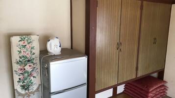 A compact room with a kitchenette area, including a refrigerator and a microwave, and a wardrobe with a wooden finish.