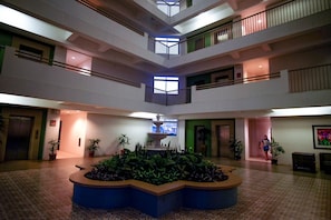 A multi-level atrium with a central fountain, potted plants, and a view of the outside through a window.