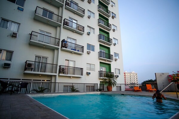 A multi-story residential building with balconies, a swimming pool, and outdoor seating. - SR Vacation Rental - Spianada Residential Condominium (Cebu City)