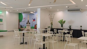 A spacious indoor area with multiple white tables and chairs arranged for dining or meetings. There are air conditioning units on the ceiling, and a mural with colorful artwork on the wall. - Go Hotels Ermita (Manila)
