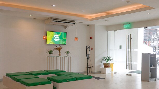 A reception area with a modern design, including a reception desk, green cushioned seating, and a large digital screen displaying the 'GO' logo. - Go Hotels Ermita (Manila)