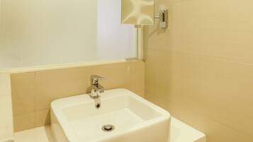 Un baño con un lavamanos blanco, un espejo y paredes cubiertas de baldosas color beige.