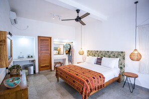Un dormitorio con cama, ventilador de techo, mesita de noche, armario y baño con lavamanos e inodoro.