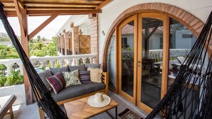 A covered outdoor seating area with a hammock, a sofa with cushions, and a view of the garden. - Abdi Hotel & Bungalow (Gili Trawangan)