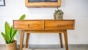 A wooden console table with two drawers, a woven basket with plants, and a television mounted on the wall. - Abdi Hotel & Bungalow (Gili Trawangan)