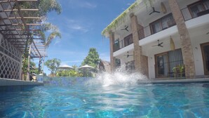 Une piscine aux eaux cristallines, avec quelques éclaboussures, entourée d’un bâtiment doté de balcons, sous un ciel dégagé.