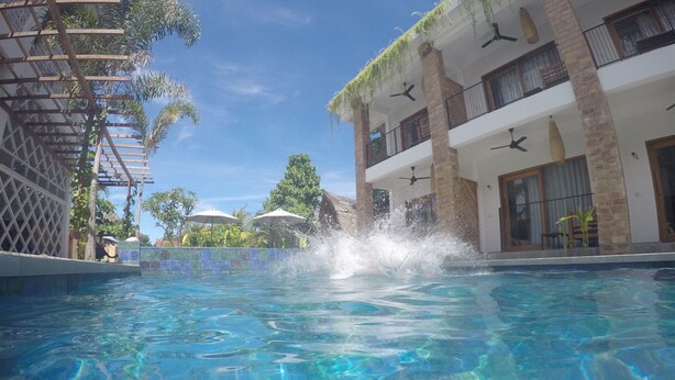 A clear swimming pool with a splash of water, surrounded by a building with balconies and a clear sky. - Abdi Hotel & Bungalow (Gili Trawangan)