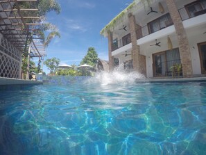 Piscina cristalina con un chapoteo de agua, rodeada por un edificio con balcones y un cielo despejado.